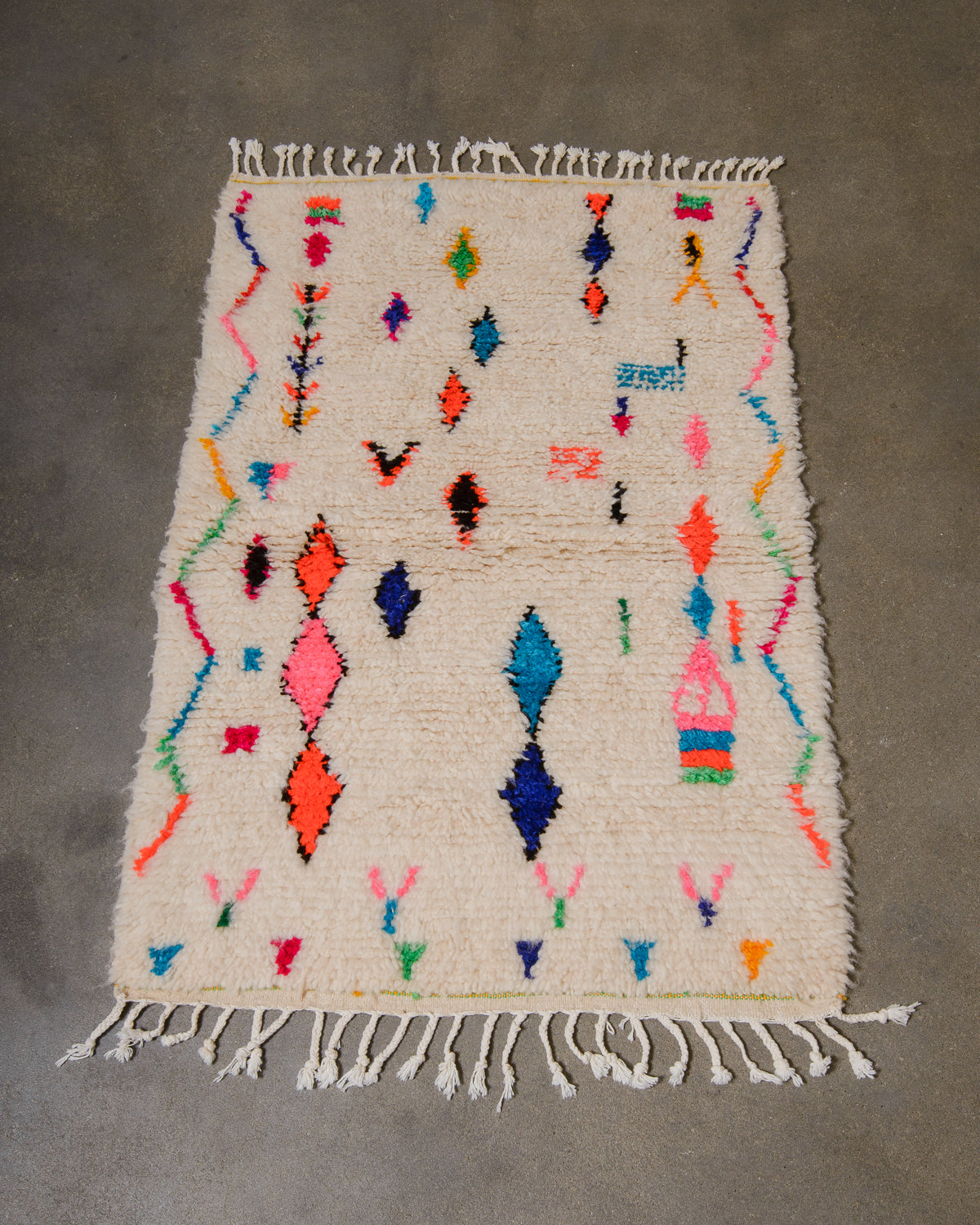 Berberlin Azilal rug in cream wool with colourful cotton laying on a grey concrete floor.